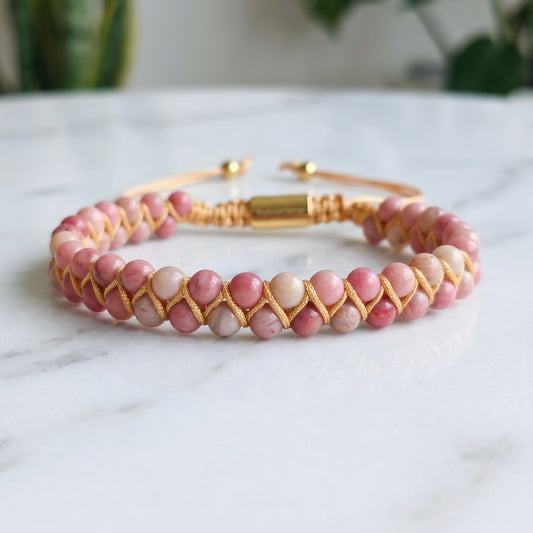 Pink Rhodonite beaded gemstone bracelet woven with gold accents on a marble surface