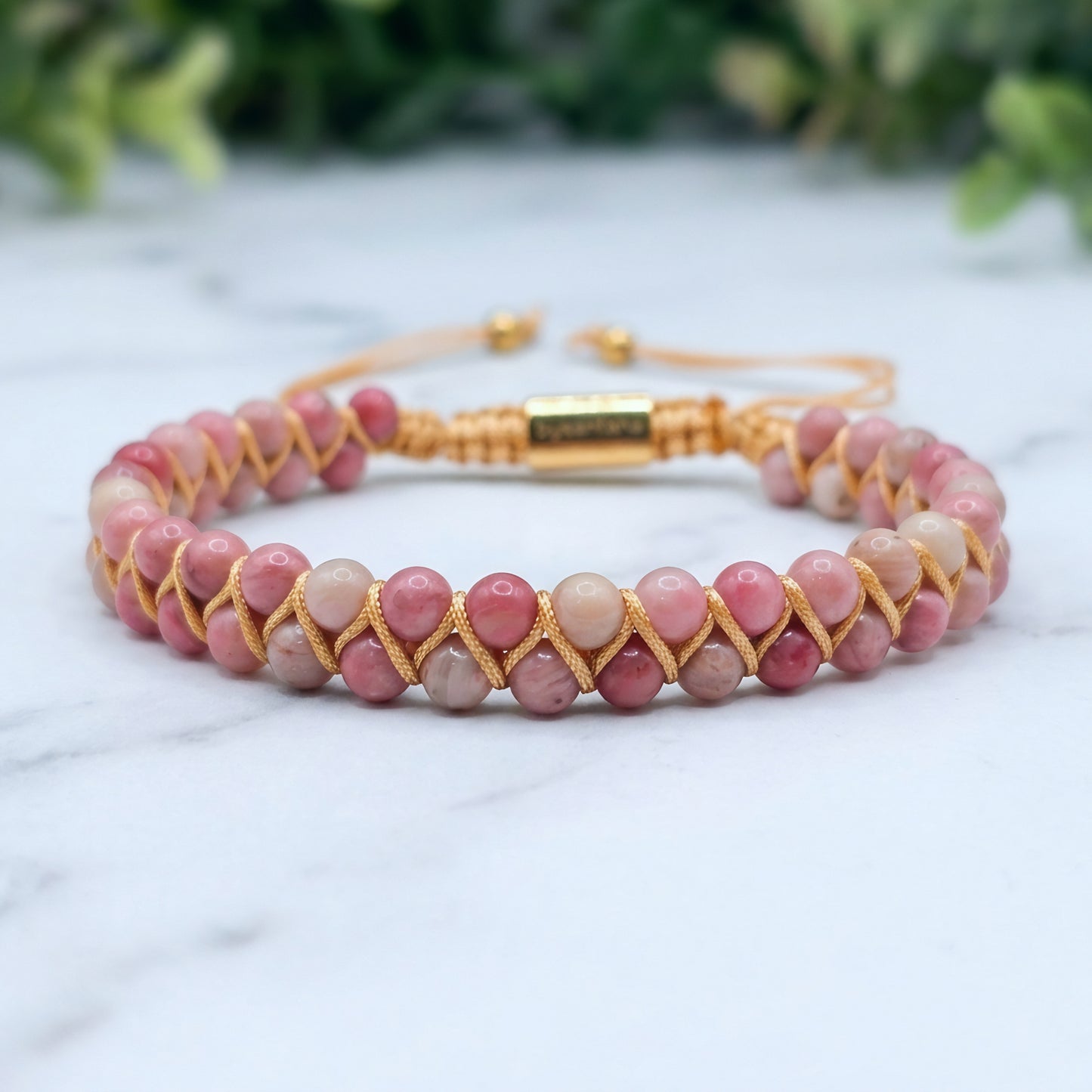 Pink Rhodonite beaded gemstone bracelet woven with gold accents on a marble surface