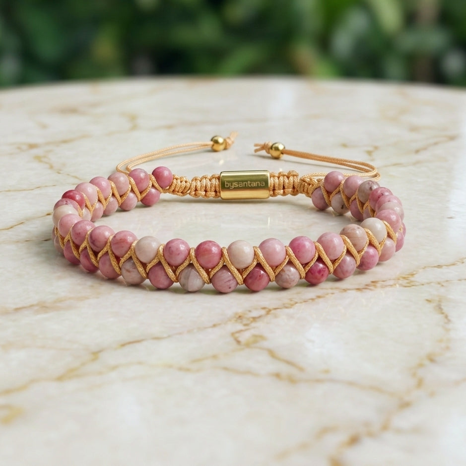 Pink Rhodonite beaded gemstone bracelet woven with gold accents on a marble surface