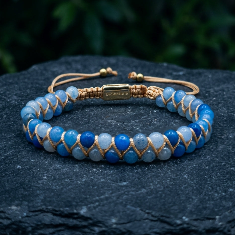 Blue aventurine beaded gemstone  bracelet with gold accents on a dark stone surface with greenery in the background