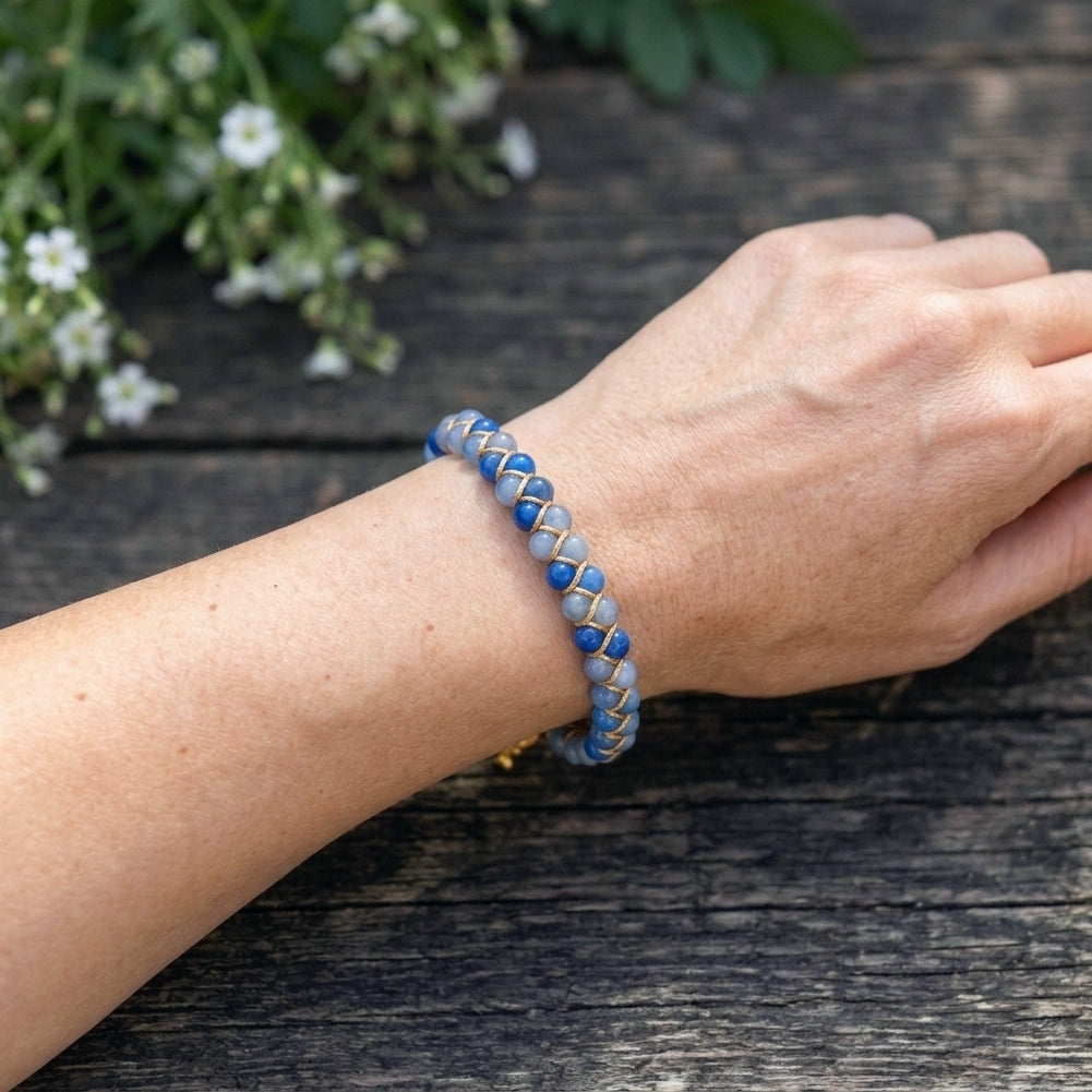 A woman's hand wearing a Blue aventurine beaded gemstone bracelet with gold accents on a wood background