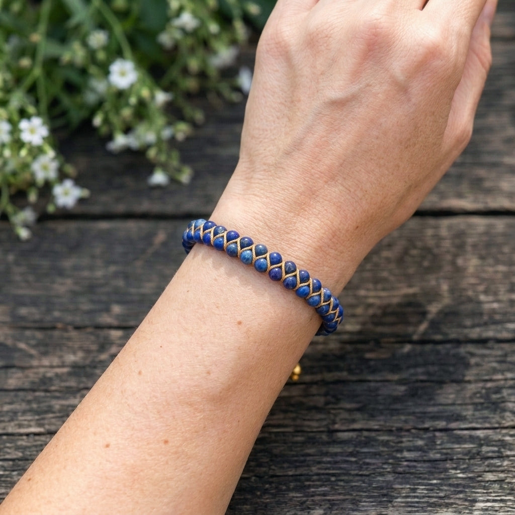 A woman's hand wearing a blue sodalite beaded bracelet on a wooden surface with white flowers in the background