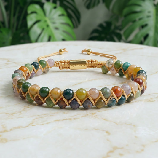 Multicolored beaded bracelet with Indian Agate gemstone beads and gold cord wrapping on a marble surface with greenery in the background