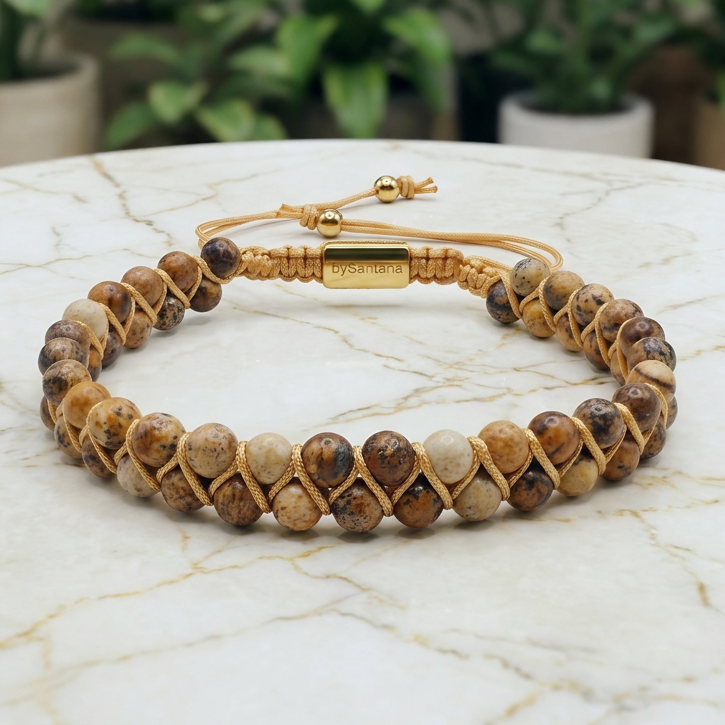 Beaded picture jasper gemstone bracelet with braided design on a marble surface with green leaves 
