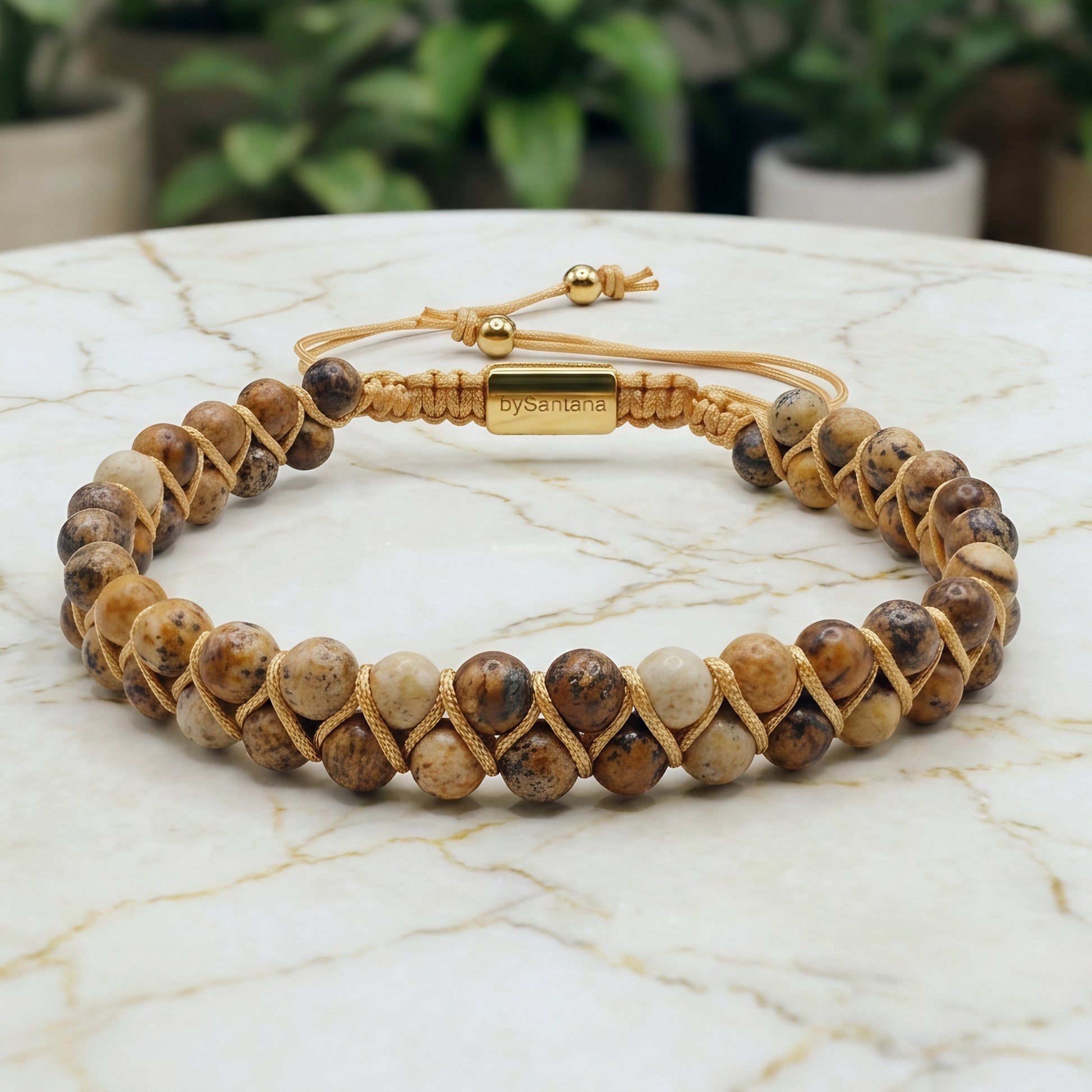 Beaded picture jasper gemstone bracelet with braided design on a marble surface with green leaves 