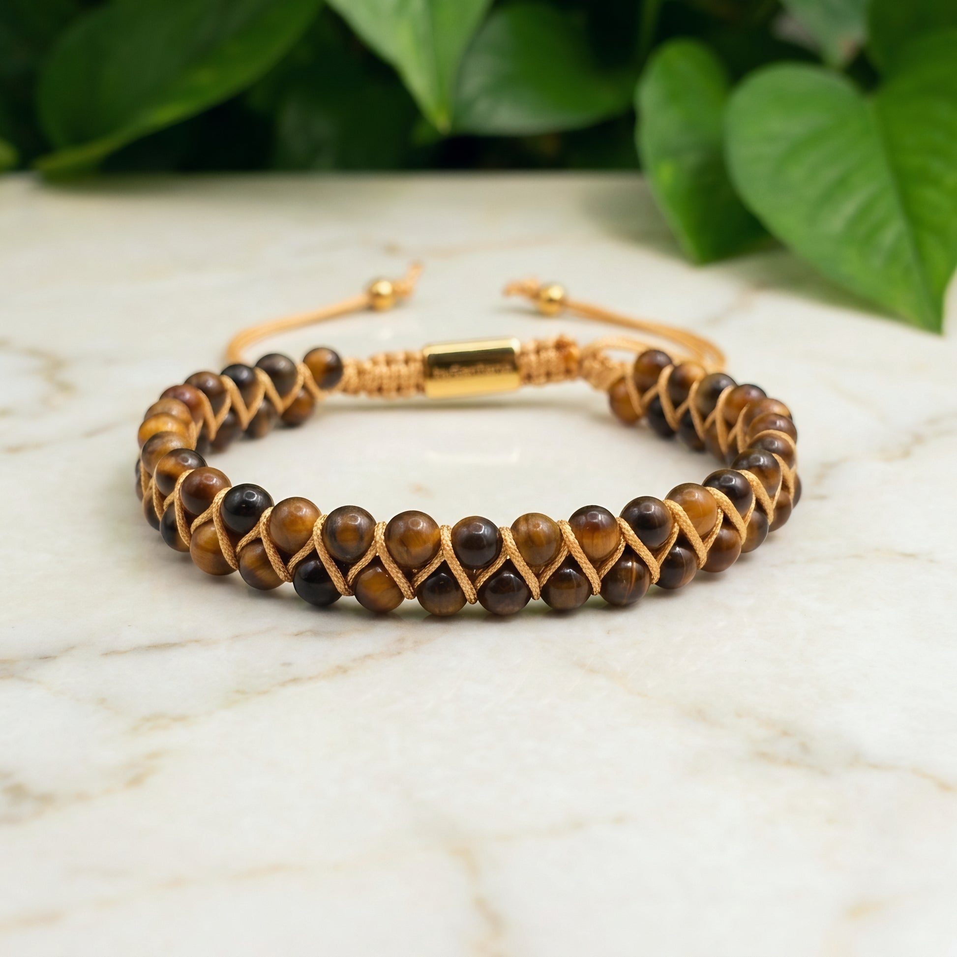 Golden Tiger's Eye beaded gemstone bracelet with gold accents on a light surface with green leaves in the background
