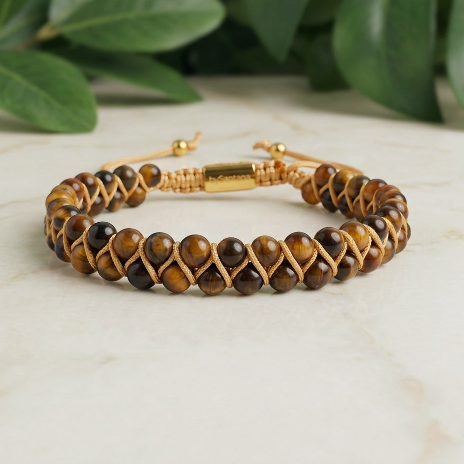 Golden Tiger's Eye beaded gemstone bracelet with gold accents on a light surface with green leaves in the background