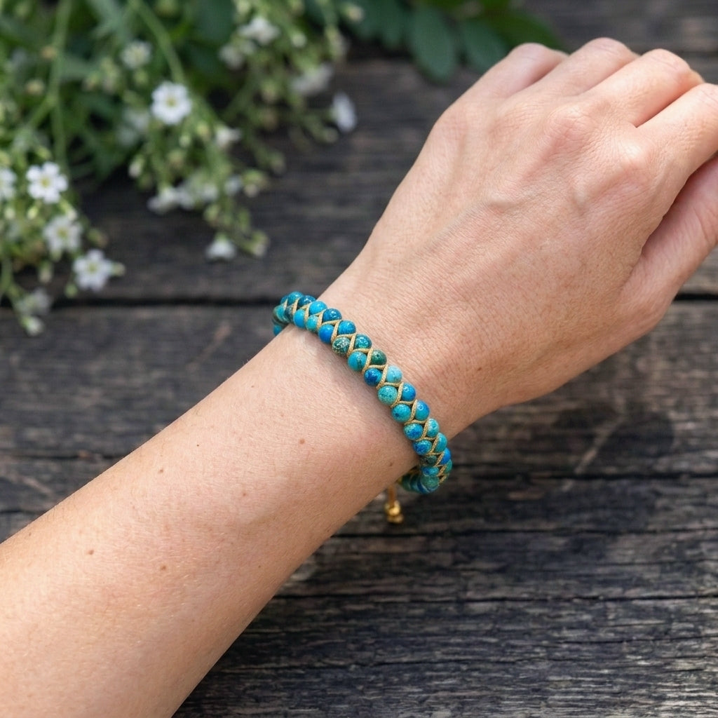 A woman's hand wearing a blue sea sediment jasper beaded gemstone bracelet on a wooden surface