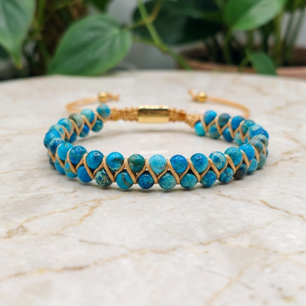 Blue sea sediment jasper beaded gemstone bracelet with gold accents on a marble surface