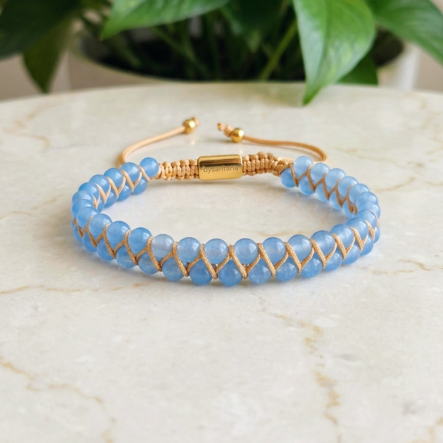 Blue aquamarine beaded gemstone bracelet with gold accents on a marble surface with green leaves.