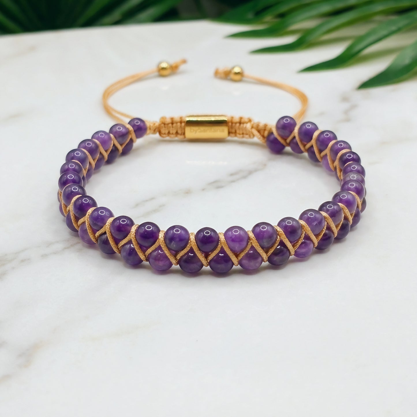 Purple Amethyst beaded gemstone adjustable bracelet with gold accents on a marble surface 