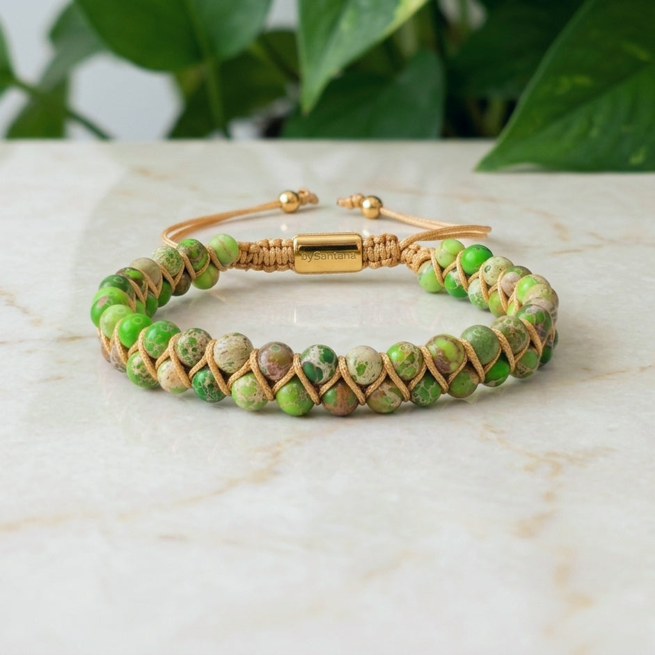 Green sea sediment jasper beaded bracelet with gold clasp on a marble surface with green leaves in the background