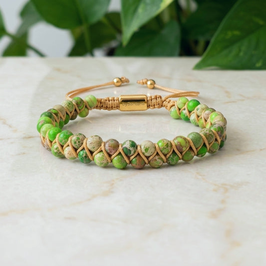 Green sea sediment jasper beaded bracelet with gold clasp on a marble surface with green leaves in the background