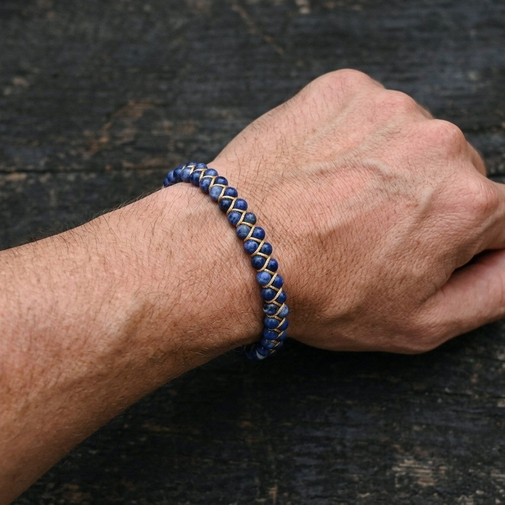 Close-up of a man's wrist wearing a blue sodalite beaded bracelet on a dark textured background