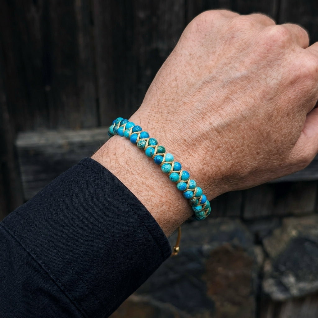 A man's hand wearing a blue sea jasper beaded bracelet with a dark background