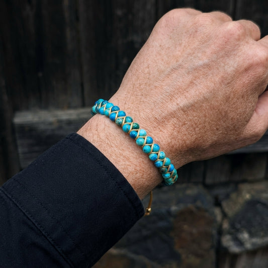 A man's hand wearing a blue sea jasper beaded bracelet with a dark background