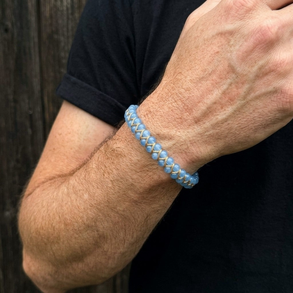 A man's arm wearing a light blue aquamarine bracelet against a dark background