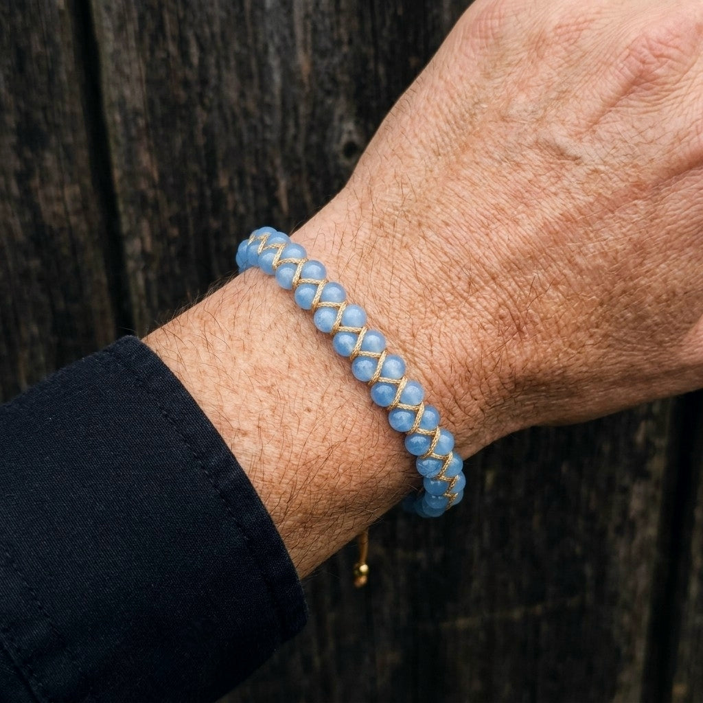 A man's wrist wearing a blue aquamarine beaded bracelet with gold accents against a wooden background.