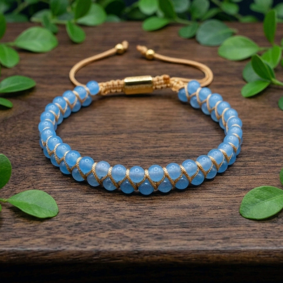 Blue aquamarine beaded gemstone bracelet with gold accents on a wooden surface with green leaves.