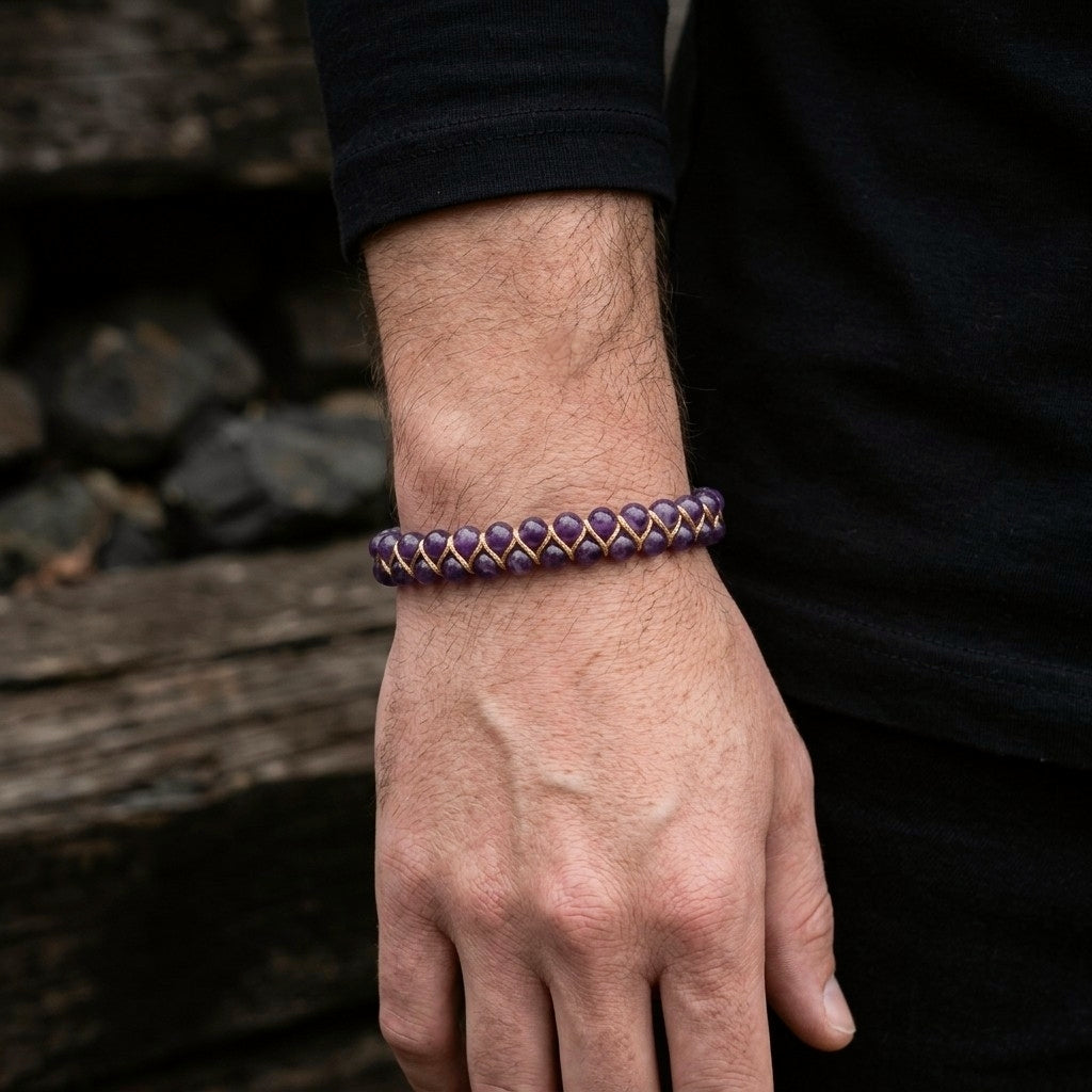 A man's hand wearing a purple Amethyst bracelet with a woven pattern against a natural background