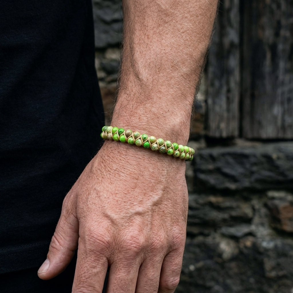 A man wearing a woven green sea sediment jasper beaded bracelet on a stone wall background