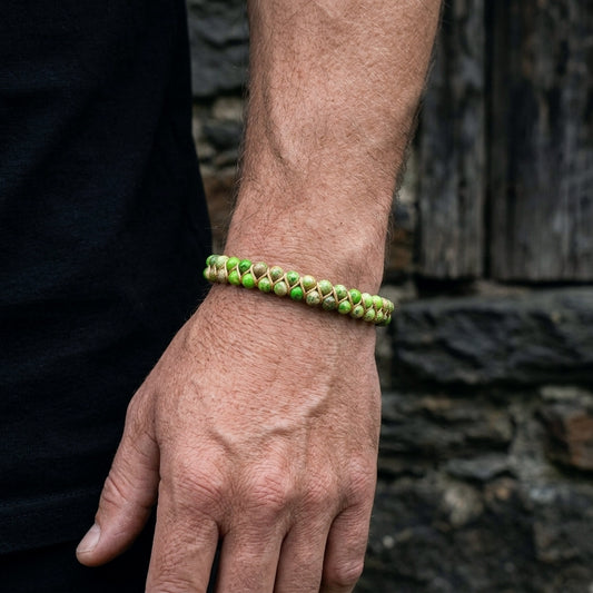 A man wearing a woven green sea sediment jasper beaded bracelet on a stone wall background