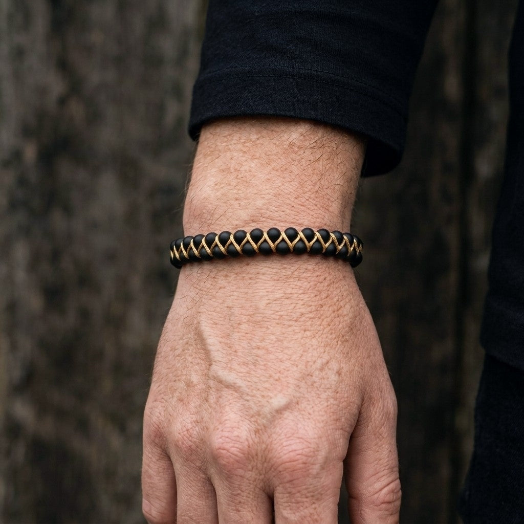 A man's hand wearing a black onyx and gold bracelet against a blurred natural background