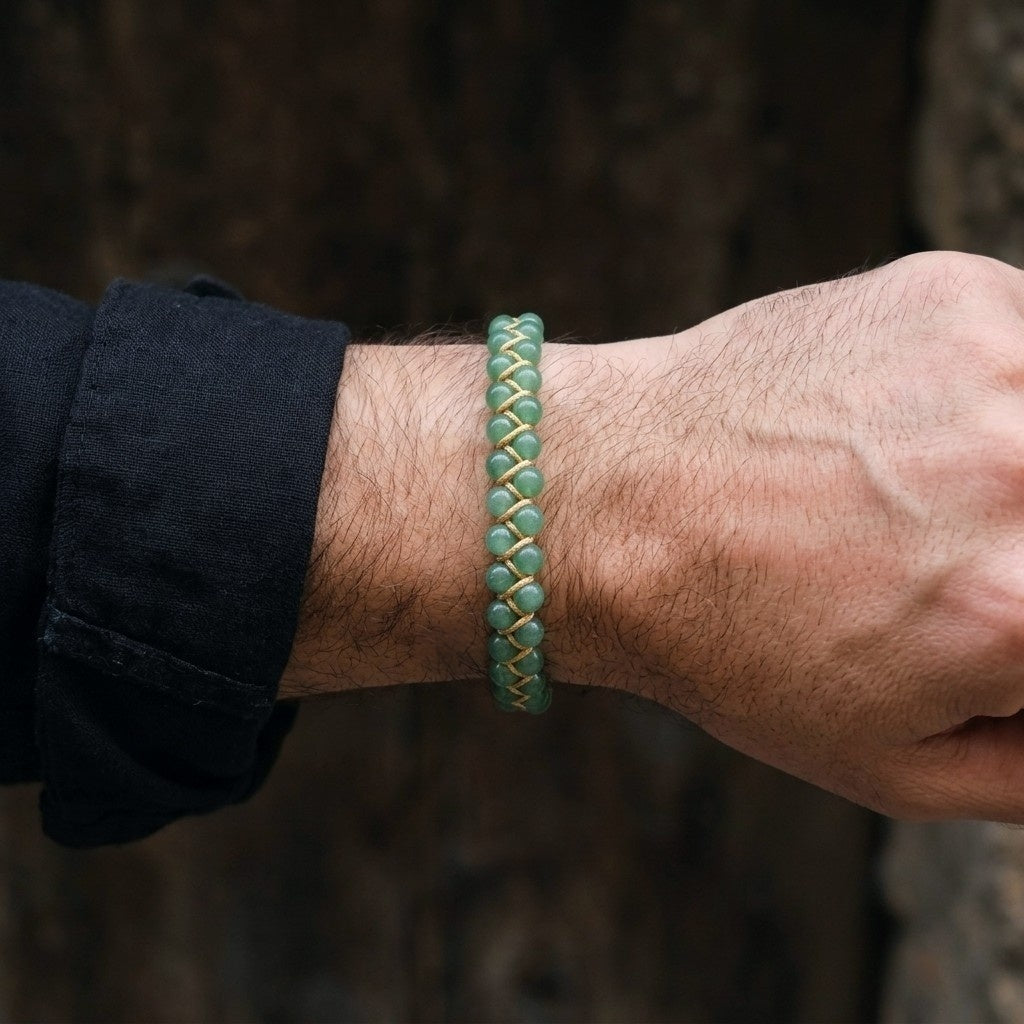 A man's hand wearing a light green aventurine beaded bracelet with a blurred natural background