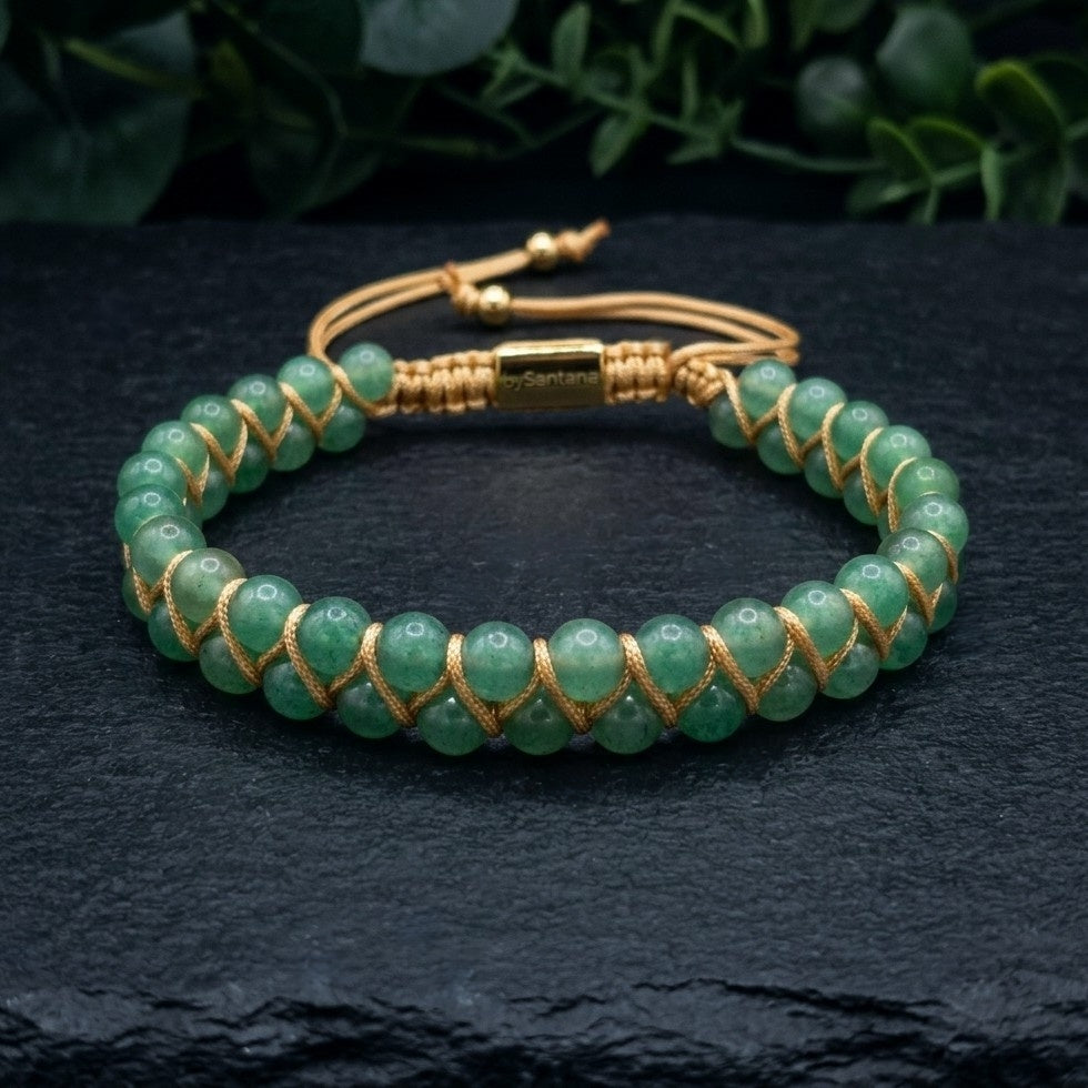 Green aventurine beaded gemstone bracelet with gold cord on a dark stone surface with green leaves in the background