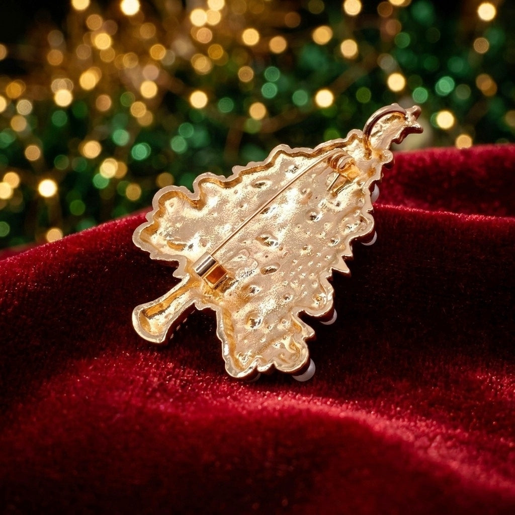 The back of a gold Christmas tree-shaped brooch showing the metal pin clasp, resting on a deep red velvet surface with a festive, blurred green and gold bokeh background.