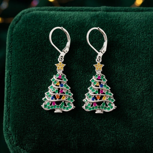 A pair of silver leverback earrings shaped like Christmas trees, decorated with green, pink, blue, yellow, and orange rhinestones, displayed on a dark green velvet jewelry box.