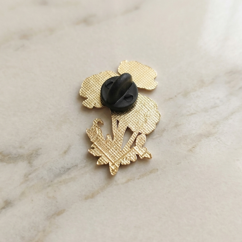 the back of a textured gold-tone metal pin with a black rubber plastic clutch fastener, resting on a light beige marble surface.