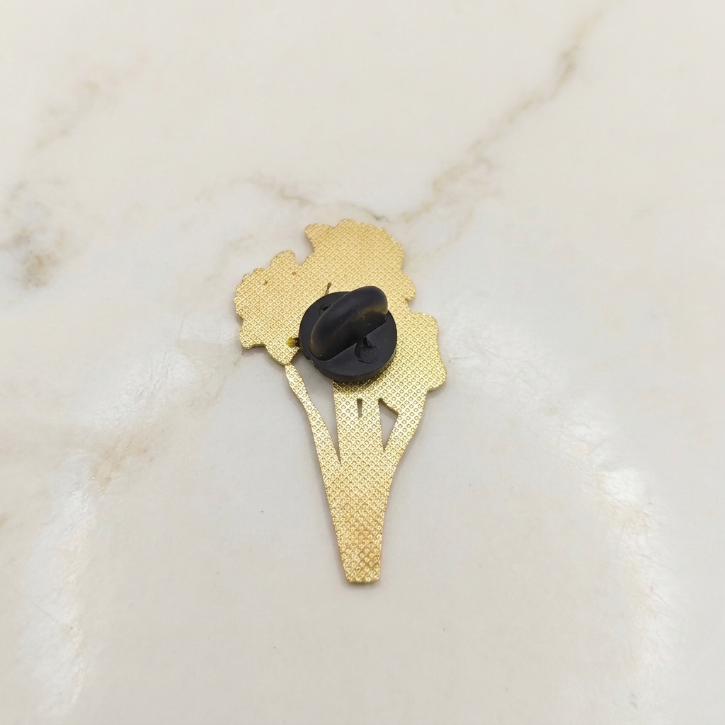 The back of a gold-colored metal pin shaped like a flower with a black plastic clutch backing, resting on a white marble surface.