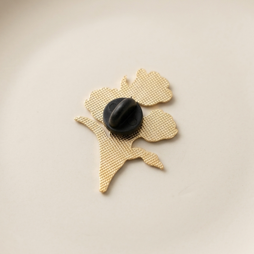 The back of a gold pin with a black rubber fastener on the back, shown on a plain off-white background.