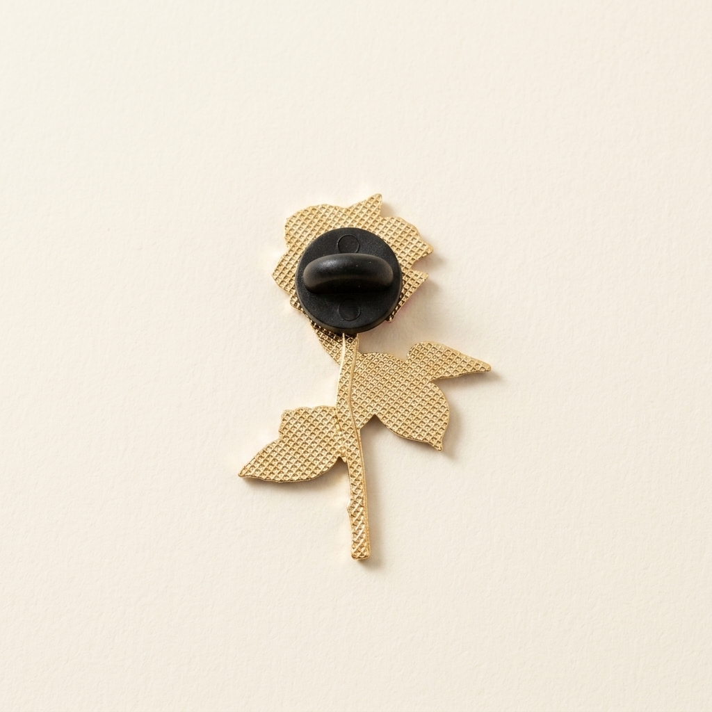 The back of a gold flower-shaped brooch with a black rubber clasp, shown on a plain off-white background.
