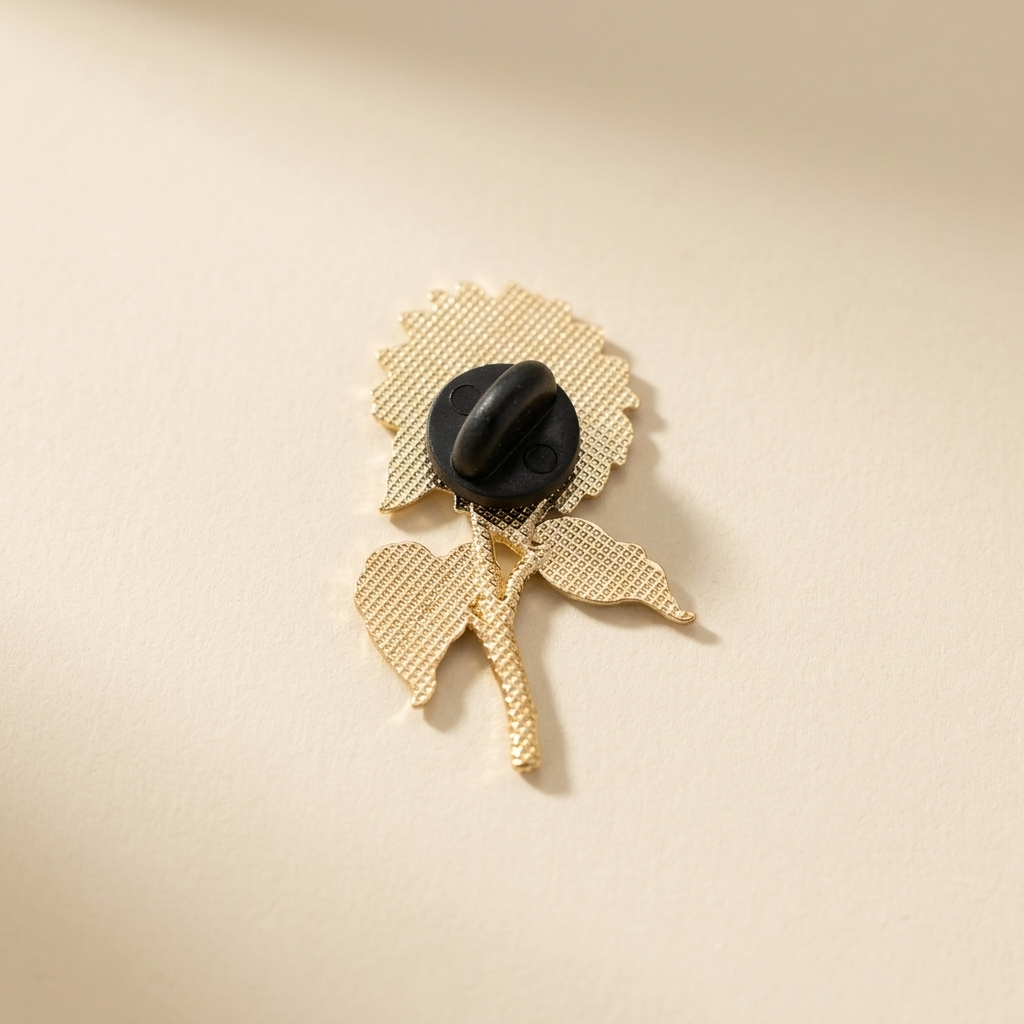 The back of a gold flower-shaped brooch with a  black rubber back, photographed on a warm cream background.