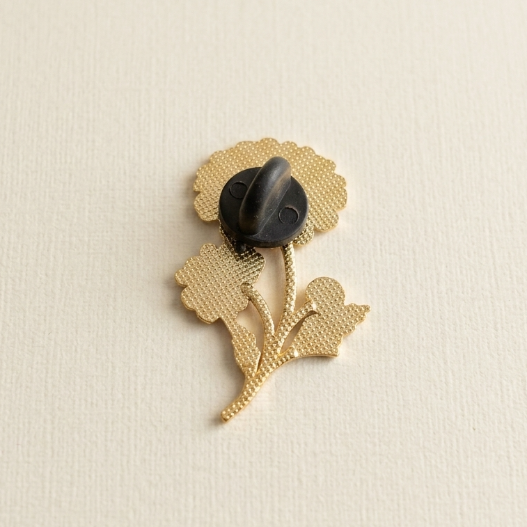 The back of a gold-tone floral brooch with a dark black rubber clasp, displayed on a light cream textured background.