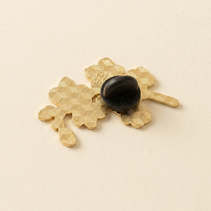 The back of a gold-toned floral brooch with a black rubber back, displayed on a warm cream background.