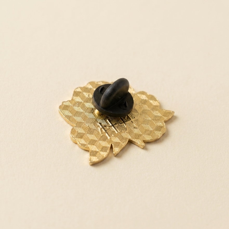 The back of a small gold pin a black plastic clasp, photographed on a plain warm beige background.