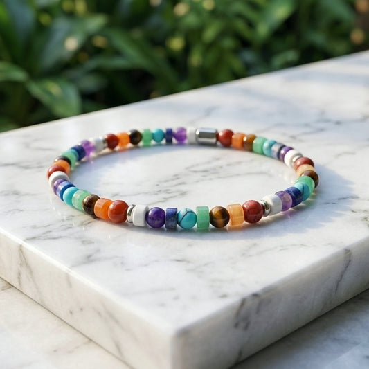 A beaded stretch bracelet with multicolored round and square natural gemstone beads, displayed on a white marble block with a blurred green garden background.