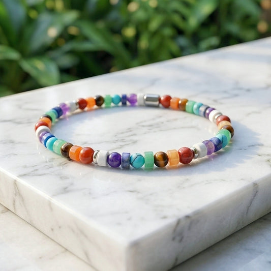A beaded stretch bracelet with multicolored round and square natural gemstone beads, displayed on a white marble block with a blurred green garden background.