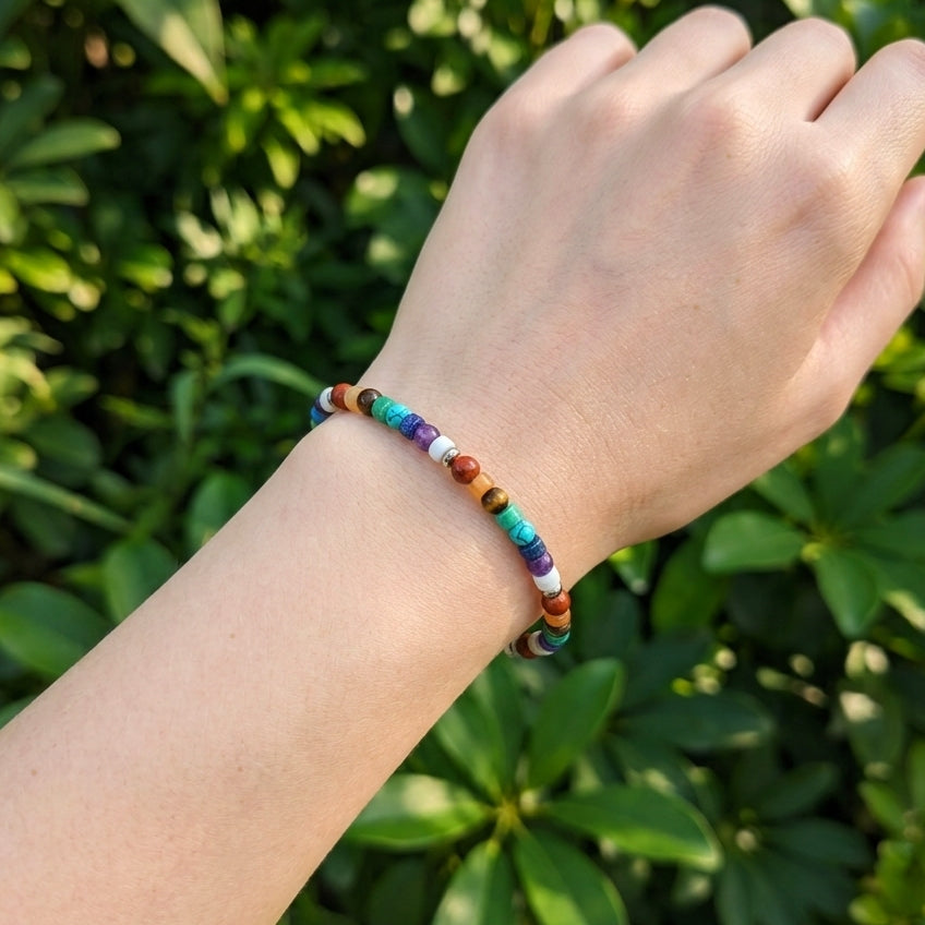A rainbow beaded bracelet worn on a person's wrist, photographed outdoors against a blurred background of green foliage.
