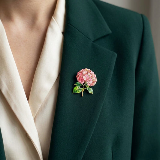 A close-up of a person wearing a dark green blazer and cream blouse, featuring a pink hydrangea brooch pinned to the lapel.