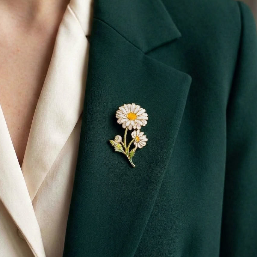 A close-up of a person wearing a dark green blazer over a cream satin blouse, featuring a delicate enamel daisy brooch pinned to the lapel.