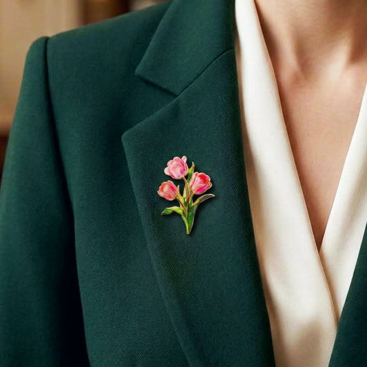 A close-up of a person wearing a dark green blazer over a cream-colored top, featuring a small pink tulip and green floral enamel pin on the lapel.