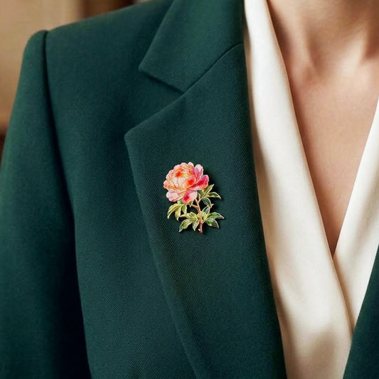 A close-up of a person wearing a dark green blazer over a cream-colored top, featuring a small pink and peach peony flower brooch with green leaves on the blazer lapel.