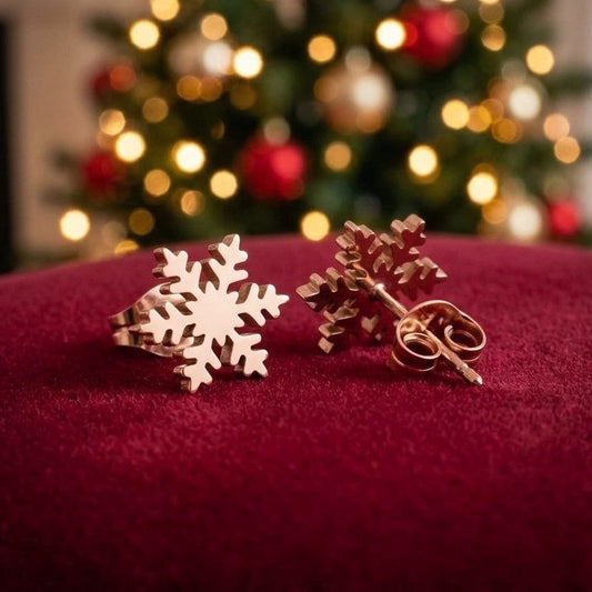 Dainty rose gold colour snowflake studs in stainless steel on red velvet with a blurred Christmas tree in the background