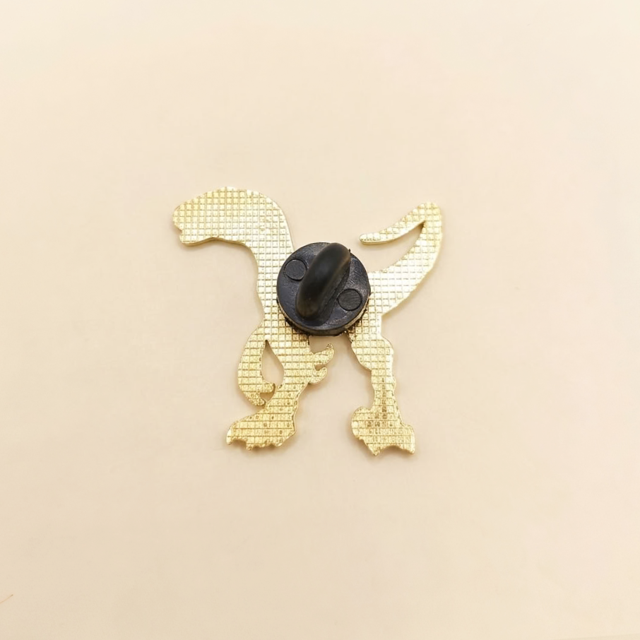 The back of a gold pin with a black plastic rubber fastener, shown on a solid beige background.