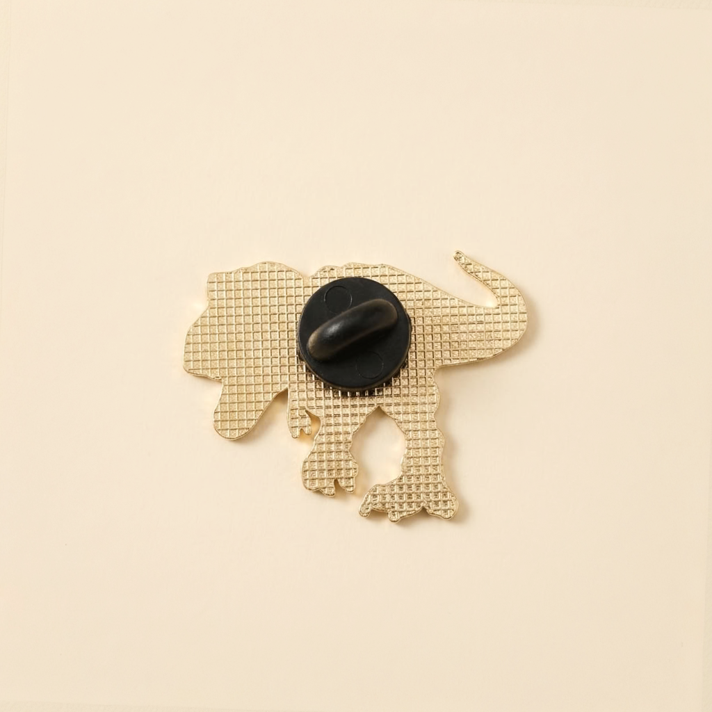 The back of a gold-toned dino-shaped pin with a a black rubber back, shown on a solid cream background.