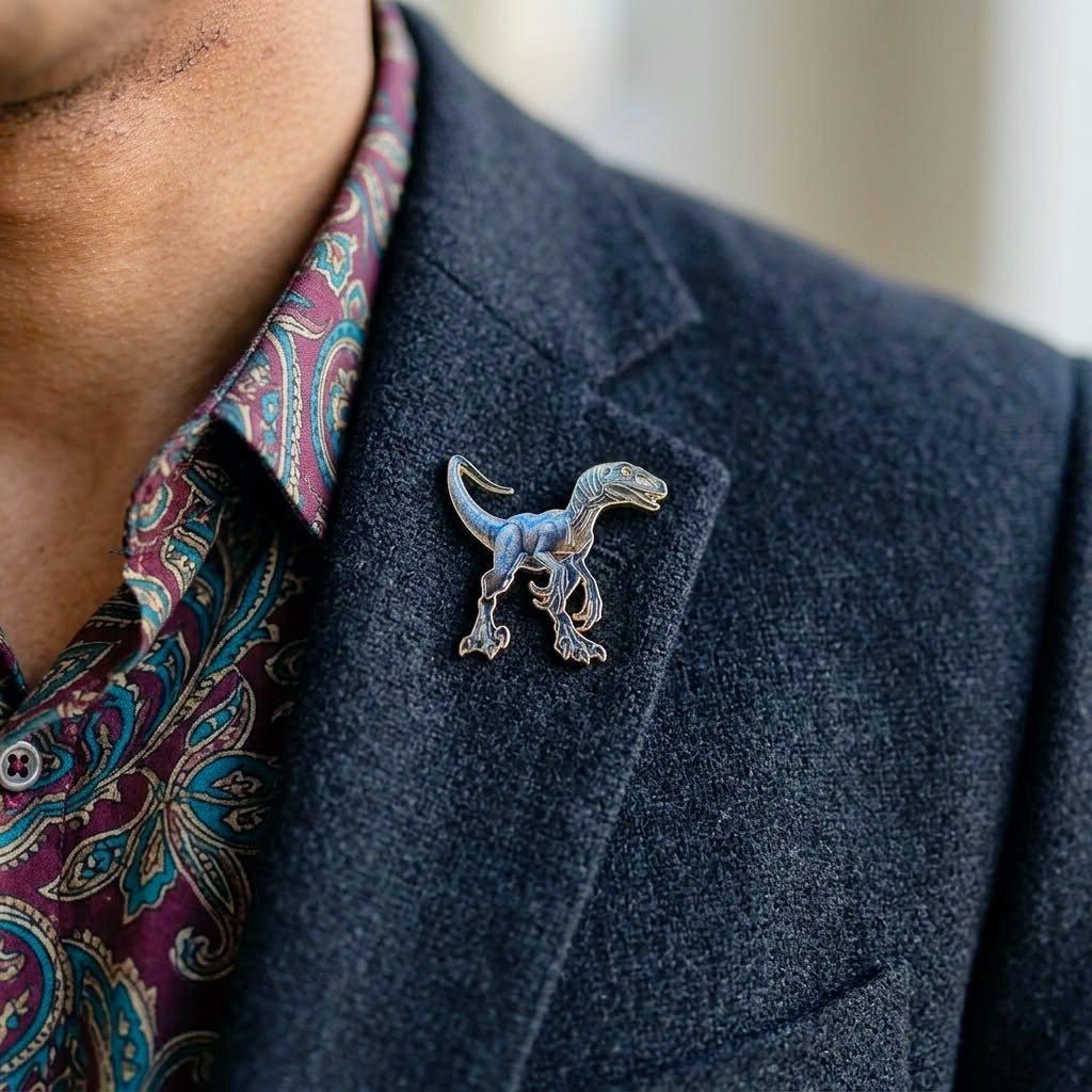 A close-up of a man wearing a dark navy blazer over a paisley shirt, featuring a small blue and gold Velociraptor dinosaur lapel pin on the blazer lapel.